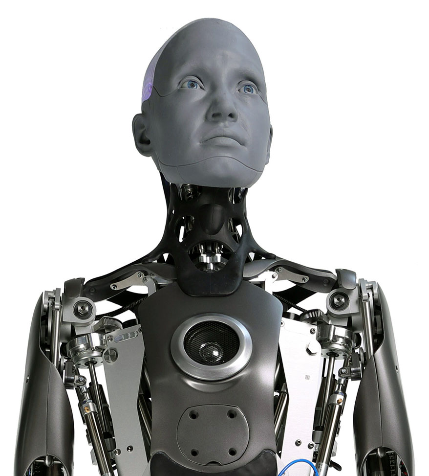Upper body of a gray humanoid robot with an expressive humanlike face, exposed neck mechanisms and a camera in its chest.