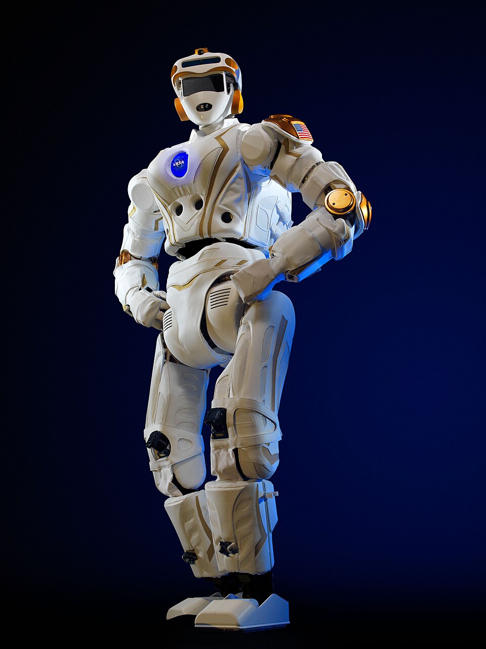 A tall white humanoid robot with orange accents and a round chest emblem posing against a dark blue background.