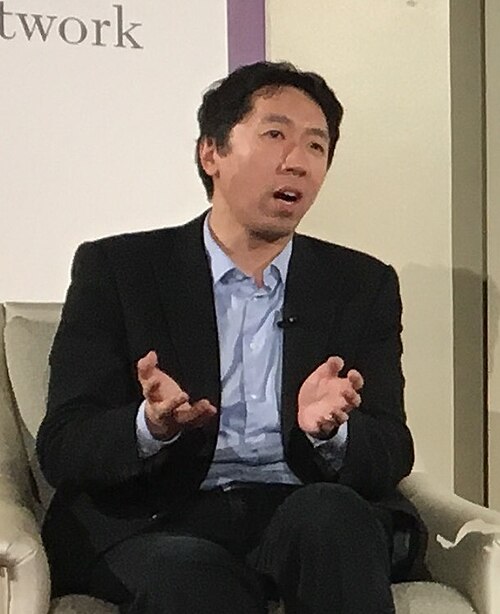 Andrew Ng seated in a dark jacket and light-blue shirt, speaking and gesturing.
