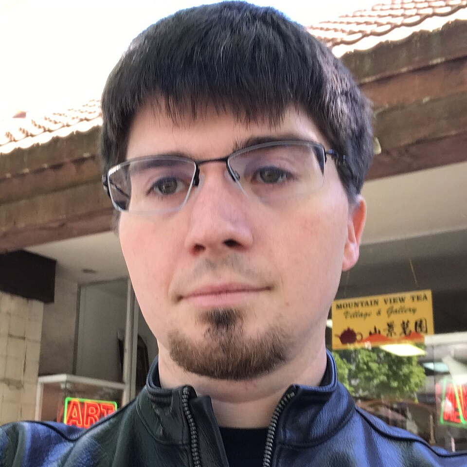 Ian Goodfellow wearing glasses and a dark zip-up jacket outdoors