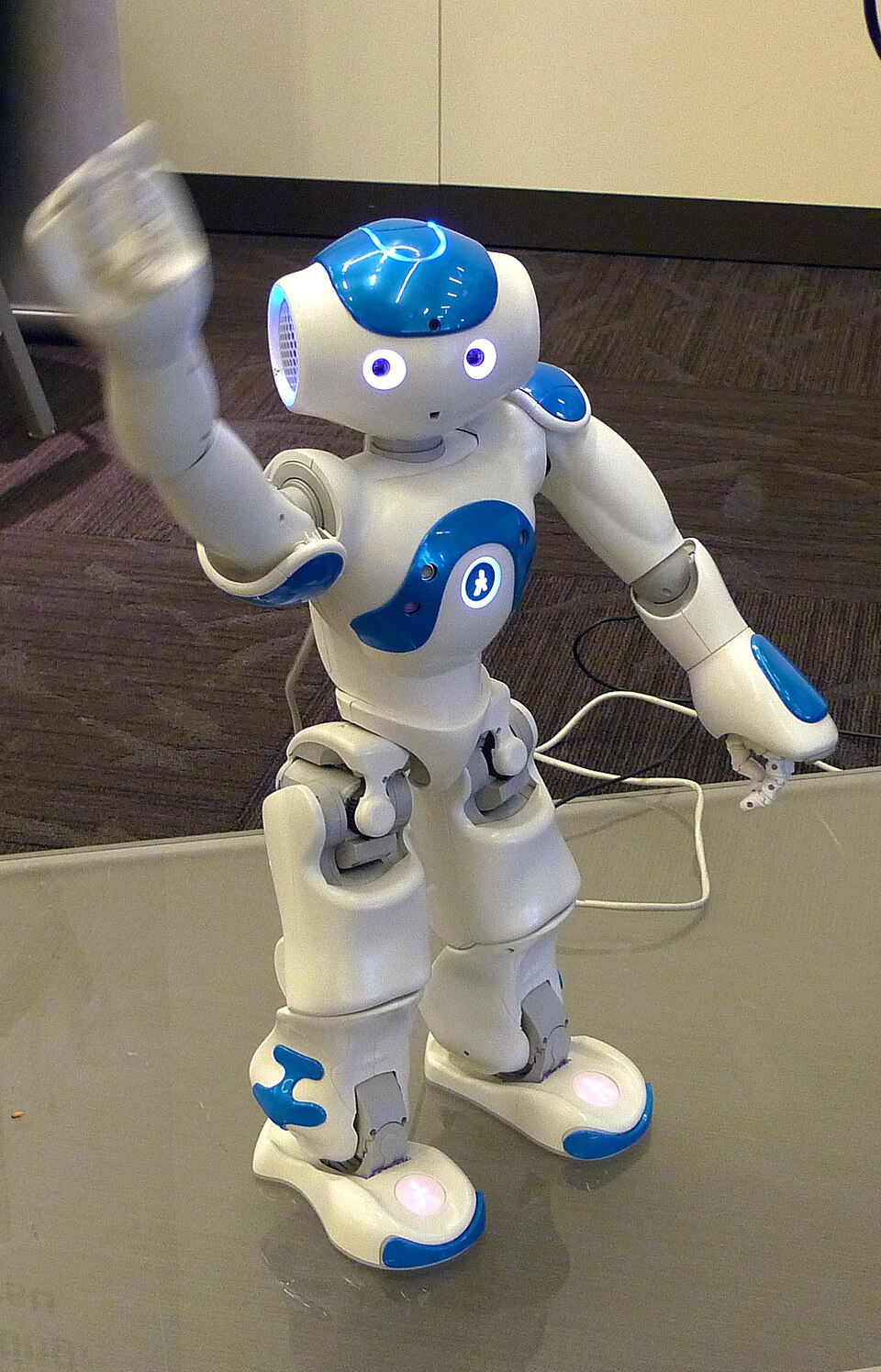 Blue and white NAO robot standing with one hand raised
