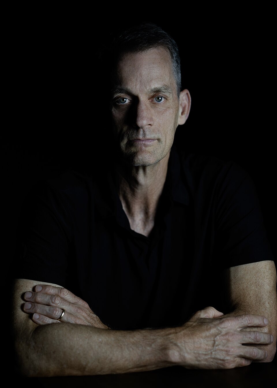 Jeff Dean wearing a black shirt, with folded arms against a dark background
