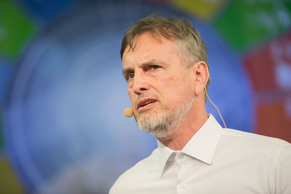 Jürgen Schmidhuber wearing a white shirt and headset microphone onstage